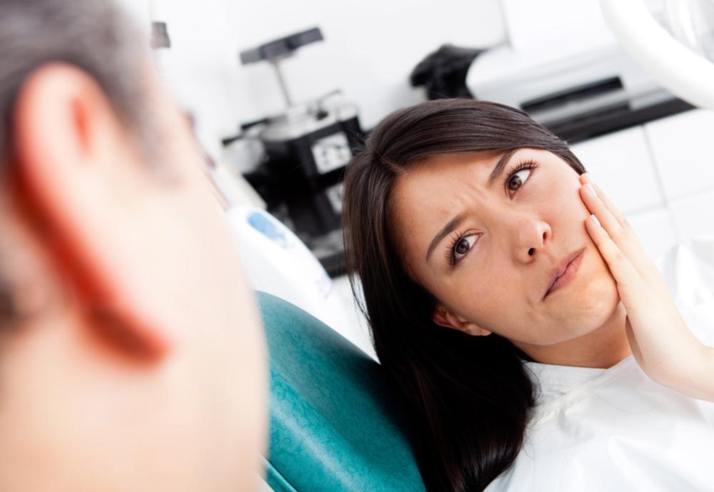 woman sitting in the dental chair holding her jaw with concern