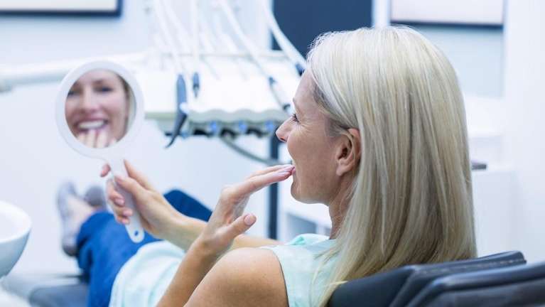 woman sitting in dentist exam chair | black triangle teeth before and after